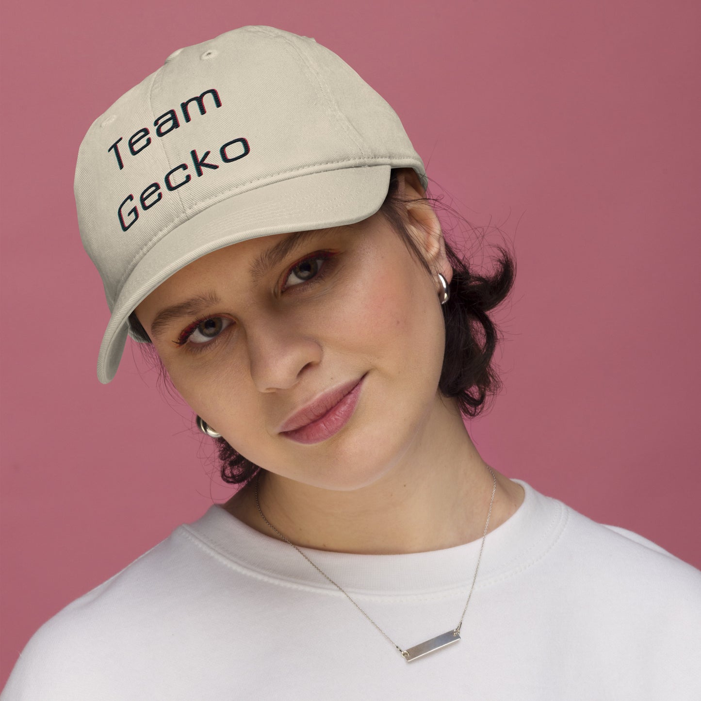 Young woman wearing oyster organic cotton baseball cap with curved bill. Team Gecko glitch text embroidered on the front. 
